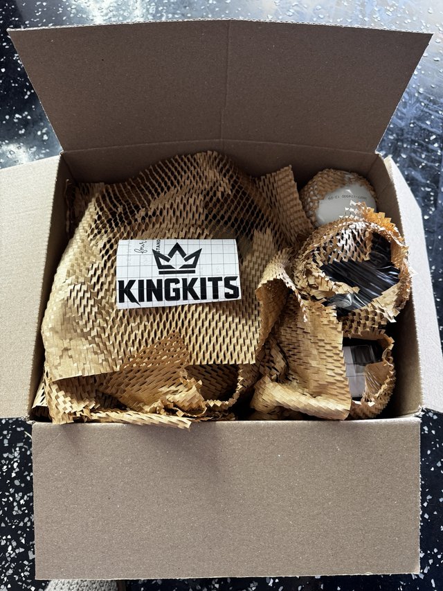 A black KingKits crown and wordmark sticker resting on protective packing inside a box.